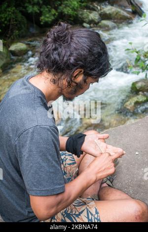 Juli 14. 2022, Himachal Pradesh Indien.. Eine Seitenpose eines jungen Mannes mit einem Mann, der ein Unkrautgelenk in den Hügeln des Himalaya rollt. Stockfoto