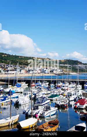 Yachten und Motorboote, die im Hafen festgemacht sind, mit Blick über die Bucht zum Strand und zur Jurassic Coastline, Lyme Regis, Dorset, UK. Stockfoto