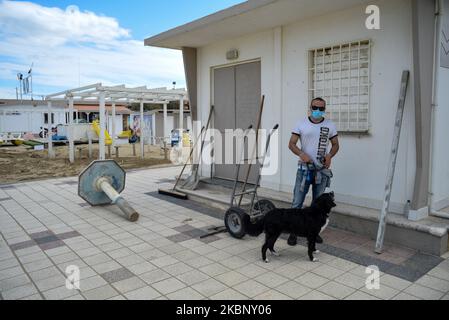 Ein Mann mit einer Gesichtsmaske geht mit seinem Hund zwischen den Badeanstalten der Riviera Romagnola, die nach dem Coronavirus-Notfall noch geschlossen sind. Rimini, Italien, 15. Mai 2020. (Foto von Andrea Savorani Neri/NurPhoto) Stockfoto