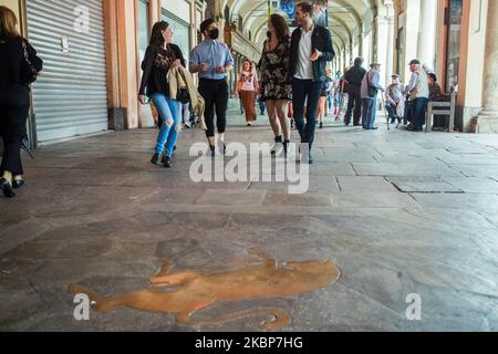 Menschen mit Schutzmaske gehen in der Nähe eines Stiers auf dem Boden, dem Symbol von Turin auf der Piazza San Carlo in Turin, Italien. Am 23. Mai konnte die Region Piemont die Tischsitze in Cafés und Bars wieder öffnen, solange die Menschen nach mehr als zwei Monaten einer landesweiten Sperre, die die Ausbreitung von COVID-19 eindämmen sollte, soziale Distanzierungen praktizieren. (Foto von Mauro Ujetto/NurPhoto) Stockfoto