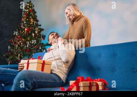 Romantisches junges Paar, das Weihnachtsgeschenke austauscht. Eine Frau schenkt einem Mann ein Geschenk. Stockfoto