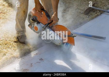 Der Bauarbeiter verwendet eine Diamanttrennsäge, um den Bürgersteig aus Beton zu schneiden Stockfoto