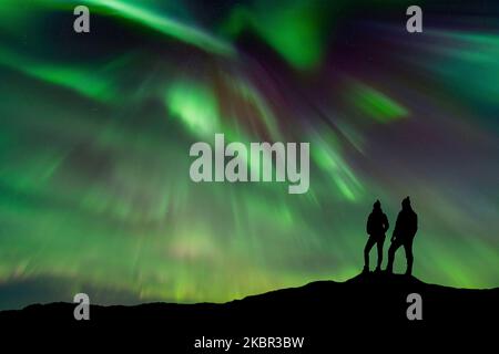 Eine Silhouette eines jungen, abenteuerlustigen Paares, das die Nordlichter, auch bekannt als aurora borealis, beobachtet Stockfoto