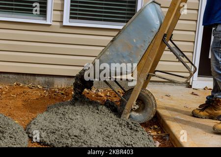 Bauarbeiter gießt Zement aus Schubkarre auf der Seite des Hauses, um Beton Bürgersteig auf Seitenhaus zu schaffen Stockfoto