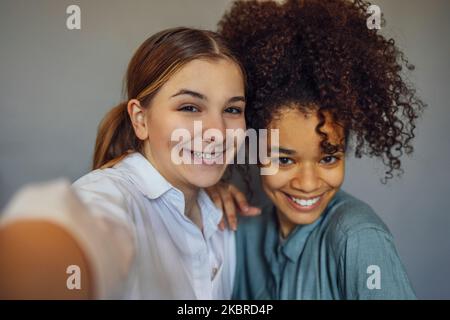 Selbstportrait von zwei fröhlichen Teenagern verschiedener Rassen, die vor der Kamera lächeln, Freundschaften genießen, multiethnische beste Freundinnen, die Selfie machen Stockfoto