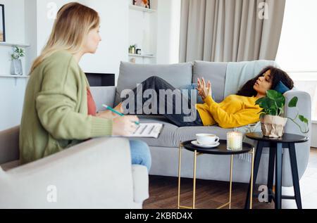 Die junge afroamerikanische Frau hat eine Sitzung mit ihrem Psychologen. Weibliche Patientin mit gemischter Rasse, die in ihrem privaten Beratungszimmer mit der Mentaltrainerin zusammenkommt Stockfoto