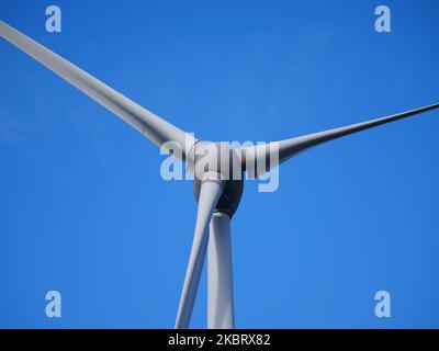 Windturbine in Nahaufnahme mit den drei Rotorblättern vor einem blauen Himmel im Hintergrund Stockfoto