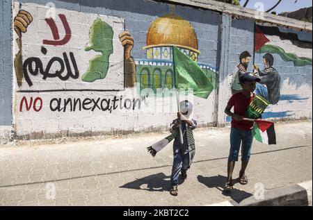 Palästinensische Jungen gehen neben ein Wandgemälde, das eine Aufklärungskampagne gegen die geplante Annexion des besetzten palästinensischen Landes durch Israel darstellt, in Rafah im südlichen Gazastreifen, am 03. Juli 2020. Der hochrangige Vertreter der Fatah-Bewegung Jibril Rajoub in der Stadt Ramallah im Westjordanland, An einer Videokonferenz nahmen wir an einem Treffen mit dem stellvertretenden Hamas-Chef Saleh Arouri Teil, bei dem er den Plan Israels diskutierte, Teile des von Israel besetzten Westjordanlands im Juli 2, 2020, zu annektieren.“ Die rivalisierenden palästinensischen Gruppierungen Fatah und Hamas versprachen Einheit gegen die Annexionspläne des Westjordanlandes. Angesichts der Besorgnis über die Ausbreitung der Diseas des Coronavirus Stockfoto