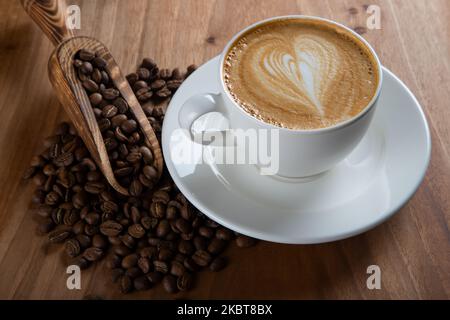 Geröstete Kaffeebohnen mit Cappuccino mit Herzschlagschaum-Muster Stockfoto