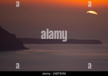 Die Sonne geht hinter dem Kameni Vulkan und der Insel Thirasia unter. Blick auf den Sonnenuntergang von Thera auf Santorini, Kykladen in der Ägäis in Griechenland. Einige Touristen und Einheimische genießen den magischen Sonnenuntergang über dem Vulkan in Fira, als das Land die Flughäfen öffnete und Touristen nach dem 1. Juli aufgrund der allgemeinen Sperrmaßnahmen des Coronavirus Covid-19, die seit Juni 15 gelockert wurden, die Möglichkeit gab, nach dem Coronavirus zu kommen. Griechenland hat vor kurzem die touristische Sommersaison wieder eröffnet, und Premierminister Kyriakos Mitsotakis hielt während des Sonnenuntergangs eine Rede von Santorin, um die touristische Saison als griechische Wirtschaft wieder in Gang zu bringen Stockfoto