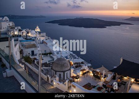 Panoramablick auf Thera mit weiß getünchten Häusern und Kirchen. Blick auf den Sonnenuntergang von Thera auf Santorini, Kykladen in der Ägäis in Griechenland. Einige Touristen und Einheimische genießen den magischen Sonnenuntergang über dem Vulkan in Fira, als das Land die Flughäfen öffnete und Touristen nach dem 1. Juli aufgrund der allgemeinen Sperrmaßnahmen des Coronavirus Covid-19, die seit Juni 15 gelockert wurden, die Möglichkeit gab, nach dem Coronavirus zu kommen. Griechenland hat vor kurzem die touristische Sommersaison wieder eröffnet, und Premierminister Kyriakos Mitsotakis hielt während des Sonnenuntergangs eine Rede von Santorin, um die touristische Saison als griechische Wirtschaft wieder in Gang zu bringen Stockfoto