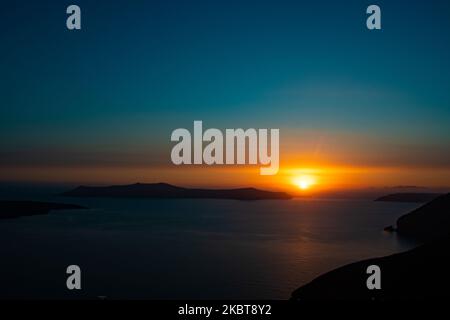 Die Sonne geht hinter dem Kameni Vulkan und der Insel Thirasia unter. Blick auf den Sonnenuntergang von Thera auf Santorini, Kykladen in der Ägäis in Griechenland. Einige Touristen und Einheimische genießen den magischen Sonnenuntergang über dem Vulkan in Fira, als das Land die Flughäfen öffnete und Touristen nach dem 1. Juli aufgrund der allgemeinen Sperrmaßnahmen des Coronavirus Covid-19, die seit Juni 15 gelockert wurden, die Möglichkeit gab, nach dem Coronavirus zu kommen. Griechenland hat vor kurzem die touristische Sommersaison wieder eröffnet, und Premierminister Kyriakos Mitsotakis hielt während des Sonnenuntergangs eine Rede von Santorin, um die touristische Saison als griechische Wirtschaft wieder in Gang zu bringen Stockfoto