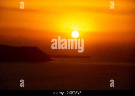 Die Sonne geht hinter dem Kameni Vulkan und der Insel Thirasia unter. Blick auf den Sonnenuntergang von Thera auf Santorini, Kykladen in der Ägäis in Griechenland. Einige Touristen und Einheimische genießen den magischen Sonnenuntergang über dem Vulkan in Fira, als das Land die Flughäfen öffnete und Touristen nach dem 1. Juli aufgrund der allgemeinen Sperrmaßnahmen des Coronavirus Covid-19, die seit Juni 15 gelockert wurden, die Möglichkeit gab, nach dem Coronavirus zu kommen. Griechenland hat vor kurzem die touristische Sommersaison wieder eröffnet, und Premierminister Kyriakos Mitsotakis hielt während des Sonnenuntergangs eine Rede von Santorin, um die touristische Saison als griechische Wirtschaft wieder in Gang zu bringen Stockfoto