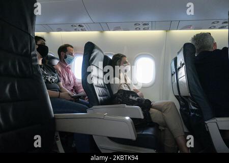 Weibliche und männliche Passagiere tragen während des Fluges Gesichtsmasken. Fliegen in einem Olympic Air De Havilland Canada DHC-8-400 Turboprop-Flugzeug während der Coronavirus-Pandemie Covid-19 mit obligatorischer Verwendung von Gesichtsmasken für die Passagiere. Die Flugbesatzung, die weibliche Flugbegleiterin, trägt auch Sicherheitsausrüstung wie Gesichtsmasken und Handschuhe, während die Mahlzeiten gewechselt werden und desinfizierende Servietten bereitgestellt werden. Die Inlandsflugstrecke führt vom Flughafen Athen ATH LGAV, der griechischen Hauptstadt, zu den Inseln der Kykladen. Griechen und ausländische Passagiere reisen nach dem G zu beliebten Inseln wie Mykonos oder Santorini Stockfoto