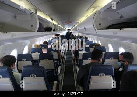 Passagiere, die in die Kabine einsteigen, müssen Gesichtsmasken verwenden. Fliegen in einem Olympic Air De Havilland Canada DHC-8-400 Turboprop-Flugzeug während der Coronavirus-Pandemie Covid-19 mit obligatorischer Verwendung von Gesichtsmasken für die Passagiere. Die Flugbesatzung, die weibliche Flugbegleiterin, trägt auch Sicherheitsausrüstung wie Gesichtsmasken und Handschuhe, während die Mahlzeiten gewechselt werden und desinfizierende Servietten bereitgestellt werden. Die Inlandsflugstrecke führt vom Flughafen Athen ATH LGAV, der griechischen Hauptstadt, zu den Inseln der Kykladen. Griechen und ausländische Passagiere reisen zu beliebten Inseln wie Mykonos oder Santorini achtern Stockfoto