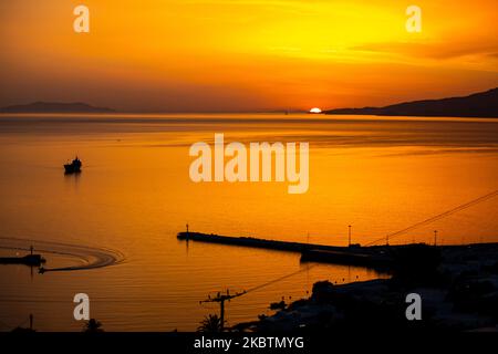 Verträumter Sonnenuntergang während der goldenen Stunde vor der Dämmerung mit dem Himmel in Rot, Orange und warmen Farben, wenn die Sonne hinter der Ägäis über Mykonos Stadt oder Chora, auf Myconos Insel in den Kykladen, Ägäis in Griechenland untergeht. Die berühmte griechische Mittelmeerinsel wird mit weiß getünchten traditionellen Gebäuden wie Windmühlen oder einer kleinen Kirche als Insel der Winde bezeichnet. Mykonos ist eine beliebte Insel für Prominente und Touristen, die im pulsierenden Nachtleben feiern möchten. Die Insel gilt auch als homosexuell freundlich. Die griechische Regierung hat die Sommersaison durch eine Lockerung der verkehrsberuhigten Straßen wieder aufgenommen Stockfoto