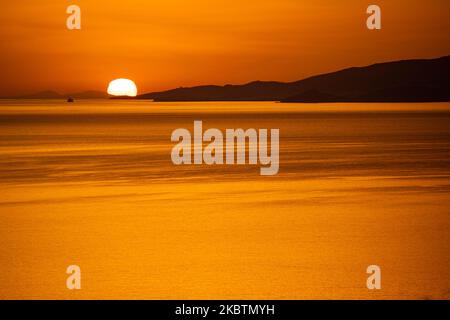 Verträumter Sonnenuntergang während der goldenen Stunde vor der Dämmerung mit dem Himmel in Rot, Orange und warmen Farben, wenn die Sonne hinter der Ägäis über Mykonos Stadt oder Chora, auf Myconos Insel in den Kykladen, Ägäis in Griechenland untergeht. Die berühmte griechische Mittelmeerinsel wird mit weiß getünchten traditionellen Gebäuden wie Windmühlen oder einer kleinen Kirche als Insel der Winde bezeichnet. Mykonos ist eine beliebte Insel für Prominente und Touristen, die im pulsierenden Nachtleben feiern möchten. Die Insel gilt auch als homosexuell freundlich. Die griechische Regierung hat die Sommersaison durch eine Lockerung der verkehrsberuhigten Straßen wieder aufgenommen Stockfoto