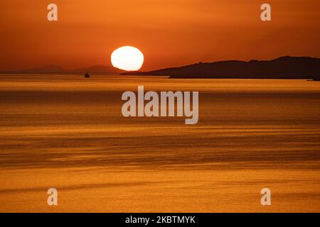 Verträumter Sonnenuntergang während der goldenen Stunde vor der Dämmerung mit dem Himmel in Rot, Orange und warmen Farben, wenn die Sonne hinter der Ägäis über Mykonos Stadt oder Chora, auf Myconos Insel in den Kykladen, Ägäis in Griechenland untergeht. Die berühmte griechische Mittelmeerinsel wird mit weiß getünchten traditionellen Gebäuden wie Windmühlen oder einer kleinen Kirche als Insel der Winde bezeichnet. Mykonos ist eine beliebte Insel für Prominente und Touristen, die im pulsierenden Nachtleben feiern möchten. Die Insel gilt auch als homosexuell freundlich. Die griechische Regierung hat die Sommersaison durch eine Lockerung der verkehrsberuhigten Straßen wieder aufgenommen Stockfoto