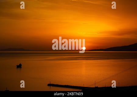 Verträumter Sonnenuntergang während der goldenen Stunde vor der Dämmerung mit dem Himmel in Rot, Orange und warmen Farben, wenn die Sonne hinter der Ägäis über Mykonos Stadt oder Chora, auf Myconos Insel in den Kykladen, Ägäis in Griechenland untergeht. Die berühmte griechische Mittelmeerinsel wird mit weiß getünchten traditionellen Gebäuden wie Windmühlen oder einer kleinen Kirche als Insel der Winde bezeichnet. Mykonos ist eine beliebte Insel für Prominente und Touristen, die im pulsierenden Nachtleben feiern möchten. Die Insel gilt auch als homosexuell freundlich. Die griechische Regierung hat die Sommersaison durch eine Lockerung der verkehrsberuhigten Straßen wieder aufgenommen Stockfoto