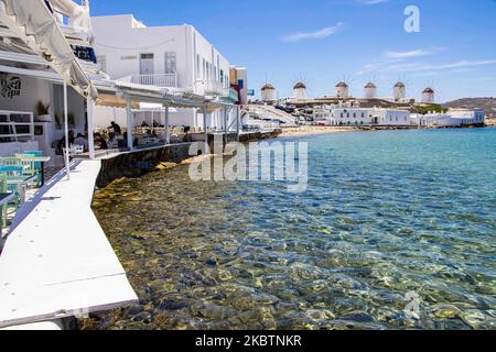 Die berühmten Windmühlen von Mykonos von Little Venice über dem Strand und das kristallklare Wasser. Die fast immer überfüllte Gegend Little Venice ist aufgrund der Coronavirus-Verkehrsbeschränkungen ohne viele Besucher. Die berühmten Windmühlen auf der Insel Mykonos, Kykladen-Inseln, Ägäis, Griechenland am 14. Juli 2020. Es gibt 16 Windmühlen auf der Insel, 5 davon oberhalb von Chora oder Mykonos Town, der Hauptstadt der Insel. Die Windmühlen wurden im 16.. Jahrhundert von den Venezianern gebaut, aber ihre Bauten dauerten bis zum 20.. Jahrhundert an. Die berühmte griechische Mittelmeerinsel wird als Spitzname bezeichnet Stockfoto