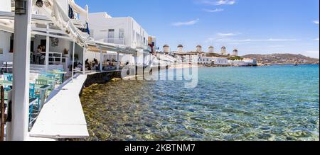 Die berühmten Windmühlen von Mykonos von Little Venice über dem Strand und das kristallklare Wasser. Die fast immer überfüllte Gegend Little Venice ist aufgrund der Coronavirus-Verkehrsbeschränkungen ohne viele Besucher. Die berühmten Windmühlen auf der Insel Mykonos, Kykladen-Inseln, Ägäis, Griechenland am 14. Juli 2020. Es gibt 16 Windmühlen auf der Insel, 5 davon oberhalb von Chora oder Mykonos Town, der Hauptstadt der Insel. Die Windmühlen wurden im 16.. Jahrhundert von den Venezianern gebaut, aber ihre Bauten dauerten bis zum 20.. Jahrhundert an. Die berühmte griechische Mittelmeerinsel wird als Spitzname bezeichnet Stockfoto