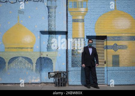 Ein Mann mit Gesichtsmaske posiert für ein Foto, während er vor einem religiösen Wandgemälde in der Nähe eines Schreines in der heiligen Stadt Qom 145km (90 Meilen) südlich von Teheran steht, nachdem am 16. März 2020 ein Covid-19-Ausbruch im Iran ausgebrochen war. Qom war die erste Stadt im Iran, in der die erste mit dem neuen Coronavirus (Covid-19) infizierte Person gefunden wurde und starb. (Foto von Morteza Nikoubazl/NurPhoto) Stockfoto