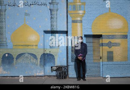 Ein Mann mit Gesichtsmaske posiert für ein Foto, während er vor einem religiösen Wandgemälde in der Nähe eines Schreines in der heiligen Stadt Qom 145km (90 Meilen) südlich von Teheran steht, nachdem am 16. März 2020 ein Covid-19-Ausbruch im Iran ausgebrochen war. Qom war die erste Stadt im Iran, in der die erste mit dem neuen Coronavirus (Covid-19) infizierte Person gefunden wurde und starb. (Foto von Morteza Nikoubazl/NurPhoto) Stockfoto