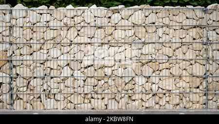 Hellbeige Natursteine sind in einer galvanisierten Gabionwand ordentlich geschichtet. Stockfoto