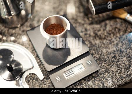 Frisch gemahlener Kaffee wird auf einer Küchenwaage in einem Aluminiumbehälter präzise gewogen. Stockfoto