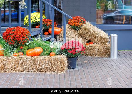 Auf den Holztreppen eines Straßencafés vor dem Eingang gibt es Kürbisse, Blumen und Strohballen für die Halloween-Feiertage. Stockfoto