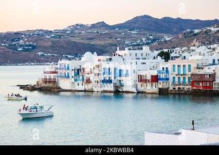 Magische Stunde bei Sonnenuntergang und Abenddämmerung in Little Venice auf Mykonos, einem der romantischsten Orte der Mittelmeerinsel am 14. Juli 2020. Dieses Viertel ist voll von eleganten und wunderschönen alten Häusern, die sich prekär am Rande der Ägäis befinden, farbenfrohe zweistöckige Gebäude im venezianischen Stil mit Holzbalkons. Diese Gebäude beherbergen heute trendige Bars, Restaurants, Galerien und mehr, aber ihr Äußeres ist immer noch einer der beliebtesten Sonnenuntergangsorte, das klassische romantische Mykonos-Erlebnis. Die berühmte Insel in den Kykladen wird als die Insel der Wi benannt Stockfoto