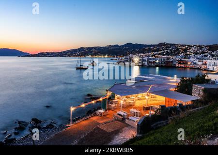 Magische Stunde bei Sonnenuntergang und Abenddämmerung in Little Venice auf Mykonos, einem der romantischsten Orte der Mittelmeerinsel am 14. Juli 2020. Dieses Viertel ist voll von eleganten und wunderschönen alten Häusern, die sich prekär am Rande der Ägäis befinden, farbenfrohe zweistöckige Gebäude im venezianischen Stil mit Holzbalkons. Diese Gebäude beherbergen heute trendige Bars, Restaurants, Galerien und mehr, aber ihr Äußeres ist immer noch einer der beliebtesten Sonnenuntergangsorte, das klassische romantische Mykonos-Erlebnis. Die berühmte Insel in den Kykladen wird als die Insel der Wi benannt Stockfoto