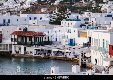 Magische Stunde bei Sonnenuntergang und Abenddämmerung in Little Venice auf Mykonos, einem der romantischsten Orte der Mittelmeerinsel am 14. Juli 2020. Dieses Viertel ist voll von eleganten und wunderschönen alten Häusern, die sich prekär am Rande der Ägäis befinden, farbenfrohe zweistöckige Gebäude im venezianischen Stil mit Holzbalkons. Diese Gebäude beherbergen heute trendige Bars, Restaurants, Galerien und mehr, aber ihr Äußeres ist immer noch einer der beliebtesten Sonnenuntergangsorte, das klassische romantische Mykonos-Erlebnis. Die berühmte Insel in den Kykladen wird als die Insel der Wi benannt Stockfoto