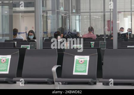 Passagiere und leere Sitzplätze mit Schildern, die sie vor dem Einsteigen im Abflugbereich blockieren. Flug vom internationalen Flughafen Mykonos JMK LGMK in Griechenland. Passagiere mit Gesichtsmasken und Schutzmaßnahmen wie Handschuhen, Händedesinfektionsmittel, Sitzblockierung, sozialen Distanzschildern usw. aufgrund der Pandemiemaßnahmen des Coronavirus Covid-19, wie sie an den Check-in-Schaltern, am Hauptabfluganschluss, an den Gates und beim Hingehen zum Flugzeug zu sehen sind, Ein Olympic Air Turboprop-Flugzeug Bombardier DHC-8-400 mit der Registrierung SX-OBA. Der Flughafen gehört der griechischen Regierung, wird aber von Fraport Greec betrieben Stockfoto