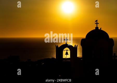 Sonnenaufgang über einer Kirche mit der Silhouette von Kuppel, Kreuz, Glocke und Vögeln. Die kleine Kapelle, wie sie am frühen Morgen auf der Vulkaninsel Santorini in den Kykladen, Ägäis in Griechenland am 6. Juli 2020 mit der Sonne vom Meer reflektiert wurde. Die griechischen Behörden hoben die Covid-19 Coronavirus-Sperrmaßnahmen auf und erlaubten die erste Touristenwelle um 15. Juni und dann seit Juli 1 mit Direktflügen zu den Inseln, aber in bestimmte Länder mit niedrigen Pandemiefällen. Die Tourismusindustrie ist eine der Haupteinnahmequellen für das Land, so dass Griechenland begann, die Maßnahmen zu lockern, um Schritt zu halten Stockfoto