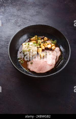 Traditioneller deutscher Schweinebraten, serviert mit Brotknödel und Königsausternpilz in dunkler Biersauce, serviert als Nahaufnahme in einer nordischen Schüssel mit C Stockfoto