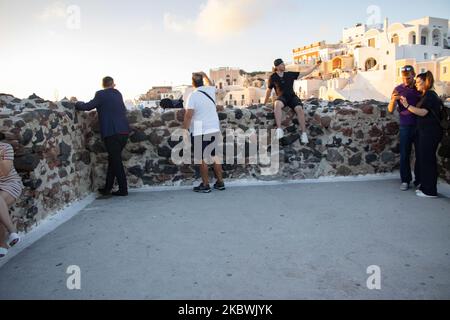 Touristen genießen den atemberaubenden Sonnenuntergang in Oia auf der Insel Santorini, auf den Kykladen, der Ägäis, in Griechenland. Sie befinden sich an einem Aussichtspunkt auf der alten traditionellen Burg und den Dächern von Häusern, Kirchen und Hotels, die auf den vulkanischen Klippen errichtet wurden. Touristen aus der ganzen Welt sind entspannt und fotografieren und Selfies mit Handys und Kameras die Sonne geht im Mittelmeer unter. Die Insel ist berühmt für den magischen Sonnenuntergang, die Architektur der weiß getünchten Häuser, Hotels mit Blick auf den Pool und die blauen Kuppelkirchen am steilen Rand der Klippe. Santorini ist ein beliebtes Ziel für Flitterwochen Stockfoto