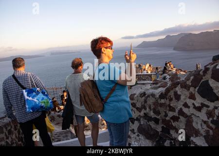 Touristen genießen den atemberaubenden Sonnenuntergang in Oia auf der Insel Santorini, auf den Kykladen, der Ägäis, in Griechenland. Sie befinden sich an einem Aussichtspunkt auf der alten traditionellen Burg und den Dächern von Häusern, Kirchen und Hotels, die auf den vulkanischen Klippen errichtet wurden. Touristen aus der ganzen Welt sind entspannt und fotografieren und Selfies mit Handys und Kameras die Sonne geht im Mittelmeer unter. Die Insel ist berühmt für den magischen Sonnenuntergang, die Architektur der weiß getünchten Häuser, Hotels mit Blick auf den Pool und die blauen Kuppelkirchen am steilen Rand der Klippe. Santorini ist ein beliebtes Ziel für Flitterwochen Stockfoto