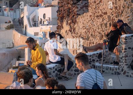 Touristen genießen den atemberaubenden Sonnenuntergang in Oia auf der Insel Santorini, auf den Kykladen, der Ägäis, in Griechenland. Sie befinden sich an einem Aussichtspunkt auf der alten traditionellen Burg und den Dächern von Häusern, Kirchen und Hotels, die auf den vulkanischen Klippen errichtet wurden. Touristen aus der ganzen Welt sind entspannt und fotografieren und Selfies mit Handys und Kameras die Sonne geht im Mittelmeer unter. Die Insel ist berühmt für den magischen Sonnenuntergang, die Architektur der weiß getünchten Häuser, Hotels mit Blick auf den Pool und die blauen Kuppelkirchen am steilen Rand der Klippe. Santorini ist ein beliebtes Ziel für Flitterwochen Stockfoto