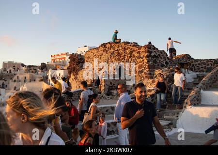 Touristen genießen den atemberaubenden Sonnenuntergang in Oia auf der Insel Santorini, auf den Kykladen, der Ägäis, in Griechenland. Sie befinden sich an einem Aussichtspunkt auf der alten traditionellen Burg und den Dächern von Häusern, Kirchen und Hotels, die auf den vulkanischen Klippen errichtet wurden. Touristen aus der ganzen Welt sind entspannt und fotografieren und Selfies mit Handys und Kameras die Sonne geht im Mittelmeer unter. Die Insel ist berühmt für den magischen Sonnenuntergang, die Architektur der weiß getünchten Häuser, Hotels mit Blick auf den Pool und die blauen Kuppelkirchen am steilen Rand der Klippe. Santorini ist ein beliebtes Ziel für Flitterwochen Stockfoto