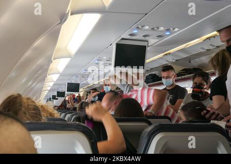 Passagiere mit Gesichtsmasken, die in einem Airbus Aegean A320 einsteigen. Fliegen in einem Aegean Airlines Airbus A320 während der Coronavirus-Pandemie mit obligatorischer Verwendung von Gesichtsmasken für die Passagiere im Flugzeug und am Flughafen. Die Flugbesatzung, die weibliche Flugbegleiterin, trägt auch Sicherheitsausrüstung wie Gesichtsmasken und Handschuhe, während die Mahlzeiten gewechselt werden und eine desinfizierende Serviette bereitgestellt wird. Die Inlandsflugroute ist von Thessaloniki SKG LGTS zum Athens ATH LGAV Airport, der griechischen Hauptstadt. Die griechische Regierung hob das Verkehrsverbot auf, sperrte Quarantänemaßnahmen für Touristen und lockert die Gattungen Stockfoto