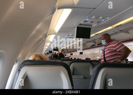 Passagiere mit Gesichtsmasken, die in einem Airbus Aegean A320 einsteigen. Fliegen in einem Aegean Airlines Airbus A320 während der Coronavirus-Pandemie mit obligatorischer Verwendung von Gesichtsmasken für die Passagiere im Flugzeug und am Flughafen. Die Flugbesatzung, die weibliche Flugbegleiterin, trägt auch Sicherheitsausrüstung wie Gesichtsmasken und Handschuhe, während die Mahlzeiten gewechselt werden und eine desinfizierende Serviette bereitgestellt wird. Die Inlandsflugroute ist von Thessaloniki SKG LGTS zum Athens ATH LGAV Airport, der griechischen Hauptstadt. Die griechische Regierung hob das Verkehrsverbot auf, sperrte Quarantänemaßnahmen für Touristen und lockert die Gattungen Stockfoto