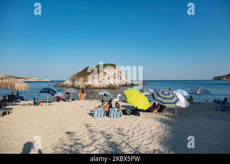 Die kleine Insel in der Nähe des Ufers von Kalamitsi. Touristenmassen am beliebten und berühmten Strand von Kalamitsi, der sich an der Südspitze der Halbinsel Sithonia in Chalkidiki in Nordgriechenland befindet. Die Menschen haben Spaß am Strand in Griechenland, wie sie unter dem Schatten der Sonnenschirme entspannen, schnorcheln, tauchen, schwimmen im tropischen exotischen kristallklaren Wasser, Wassersport treiben, Boote mieten, Bei einem Drink an den Strandbars oder beim Sonnenbaden am goldenen Sand und beim Genießen des Strandlebens unter dem sonnigen blauen Himmel. Es gibt auch eine kleine Insel in der Nähe des Ufers. Die lokalen regieren Stockfoto