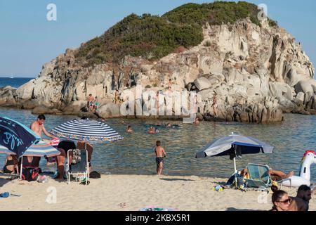 Die kleine Insel in der Nähe des Ufers von Kalamitsi. Touristenmassen am beliebten und berühmten Strand von Kalamitsi, der sich an der Südspitze der Halbinsel Sithonia in Chalkidiki in Nordgriechenland befindet. Die Menschen haben Spaß am Strand in Griechenland, wie sie unter dem Schatten der Sonnenschirme entspannen, schnorcheln, tauchen, schwimmen im tropischen exotischen kristallklaren Wasser, Wassersport treiben, Boote mieten, Bei einem Drink an den Strandbars oder beim Sonnenbaden am goldenen Sand und beim Genießen des Strandlebens unter dem sonnigen blauen Himmel. Es gibt auch eine kleine Insel in der Nähe des Ufers. Die lokalen regieren Stockfoto