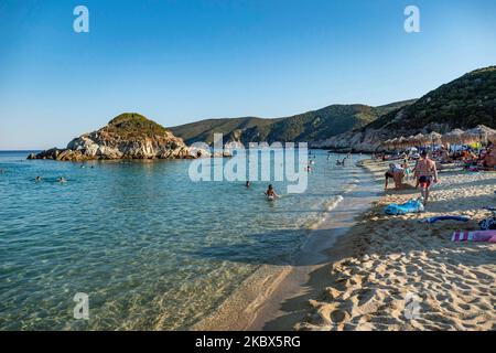 Die kleine Insel in der Nähe des Ufers von Kalamitsi. Touristenmassen am beliebten und berühmten Strand von Kalamitsi, der sich an der Südspitze der Halbinsel Sithonia in Chalkidiki in Nordgriechenland befindet. Die Menschen haben Spaß am Strand in Griechenland, wie sie unter dem Schatten der Sonnenschirme entspannen, schnorcheln, tauchen, schwimmen im tropischen exotischen kristallklaren Wasser, Wassersport treiben, Boote mieten, Bei einem Drink an den Strandbars oder beim Sonnenbaden am goldenen Sand und beim Genießen des Strandlebens unter dem sonnigen blauen Himmel. Es gibt auch eine kleine Insel in der Nähe des Ufers. Die lokalen regieren Stockfoto