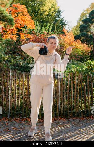 Schöne junge Frau macht Fotos mit einer professionellen Kamera im Herbstwald. Lächelndes Mädchen genießen Herbstwetter. Ruhe, Entspannung, Lifestyle Stockfoto