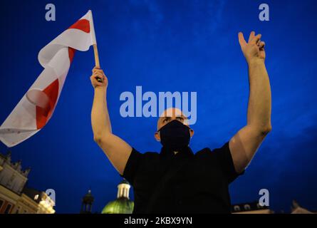 Während der weißrussischen Nationalhymne hält ein Protestler eine weiß-rot-weiße weißrussische Oppositionsflagge. Mitglieder der lokalen belarussischen Diaspora, Aktivisten und lokale Unterstützer trafen sich am Dienstagabend, um ihre Solidarität mit den belarussischen Menschen während des Protestes „Solidarität mit Belarus“, der auf dem Hauptmarkt in Krakau organisiert wurde, auszudrücken. Am 18. August 2020 in Krakau, Polen. (Foto von Artur Widak/NurPhoto) Stockfoto