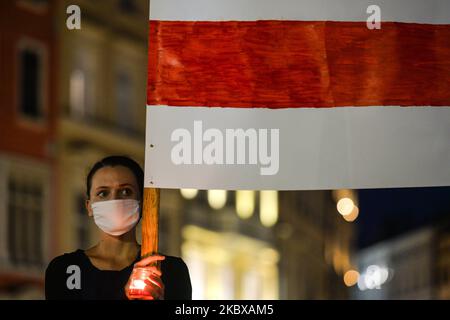 Während der weißrussischen Nationalhymne hält ein Protestler eine weiß-rot-weiße weißrussische Oppositionsflagge. Mitglieder der lokalen belarussischen Diaspora, Aktivisten und lokale Unterstützer trafen sich am Dienstagabend, um ihre Solidarität mit den belarussischen Menschen während des Protestes „Solidarität mit Belarus“, der auf dem Hauptmarkt in Krakau organisiert wurde, auszudrücken. Am 18. August 2020 in Krakau, Polen. (Foto von Artur Widak/NurPhoto) Stockfoto