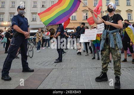 Ein Pro-LGBT-Protestler, der neben einem Polizeibeamten steht, hält während des Protestes eine Regenbogenfahne. Rechtsextreme Nationalisten und Pro-Life-Aktivisten organisierten einen Protest gegen den LGBT neben dem Adam-Mickiewicz-Denkmal auf dem Krakauer Hauptmarkt. Auf der gegenüberliegenden Seite des Platzes organisierten LGBT-Aktivisten und Antifaschisten einen Gegenprotest. Am 19. August 2020 in Krakau, Woiwodschaft Kleinpolen, Polen. (Foto von Artur Widak/NurPhoto) Stockfoto