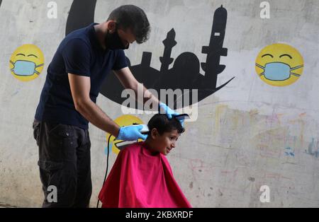 Ein palästinensischer Barbier schneidet einem Kunden auf der Straße mit Gesichtsmaske und Handschuhen die Haare, während andere während der Sperre in Gaza-Stadt am 30. August 2020, während einer Sperre in der palästinensischen Enklave aufgrund der zunehmenden Fälle von Covid-19-Coronavirus-Infektionen, an der Reihe sind. (Foto von Majdi Fathi/NurPhoto) Stockfoto